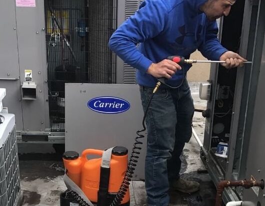 An HVAC technician doing maintenance on a roof-top condensing unit