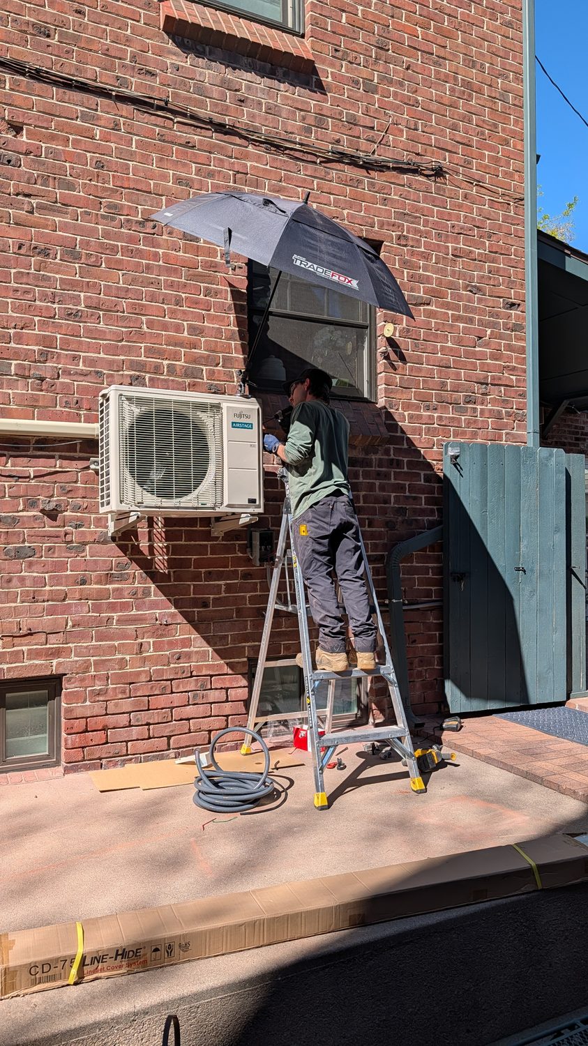 Technician on a ladder mounting an outdoor mini-split unit on brick