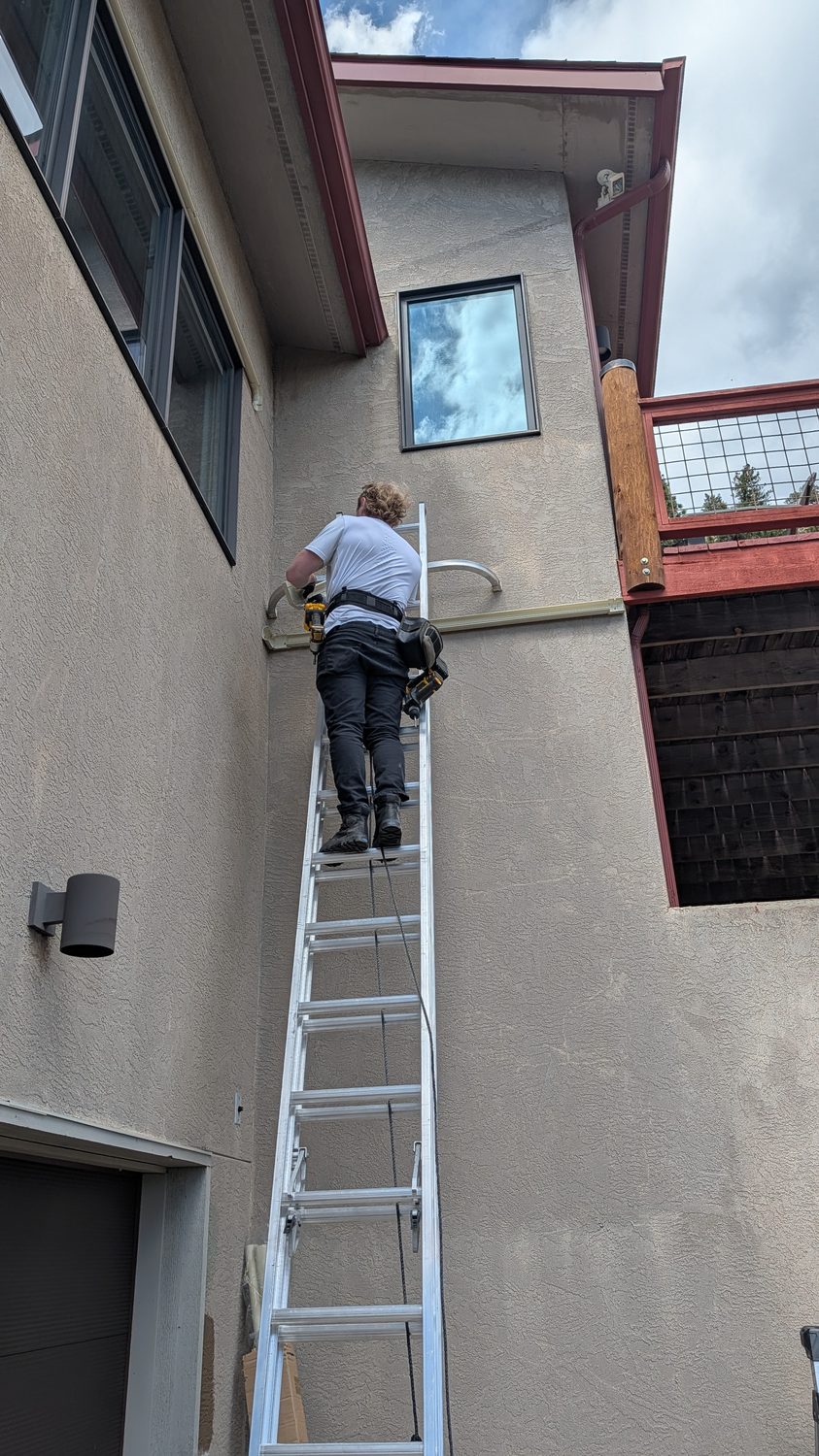 Technician running a refrigerant line set on an exterior wall