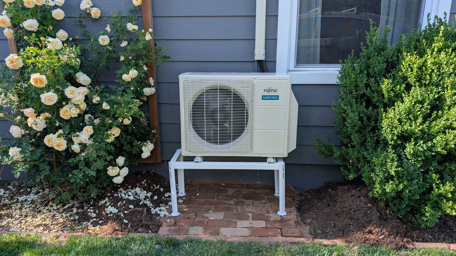 Clean outdoor mini-split condenser beside landscaped roses