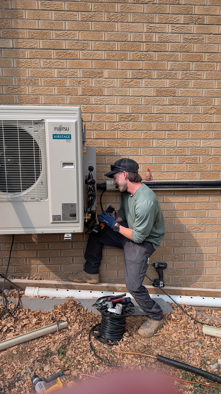 Technician servicing an outdoor mini-split unit against a brick wall